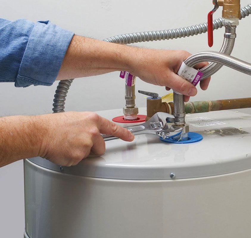 Hands using a wrench to connect pipes on a water heater tank.
