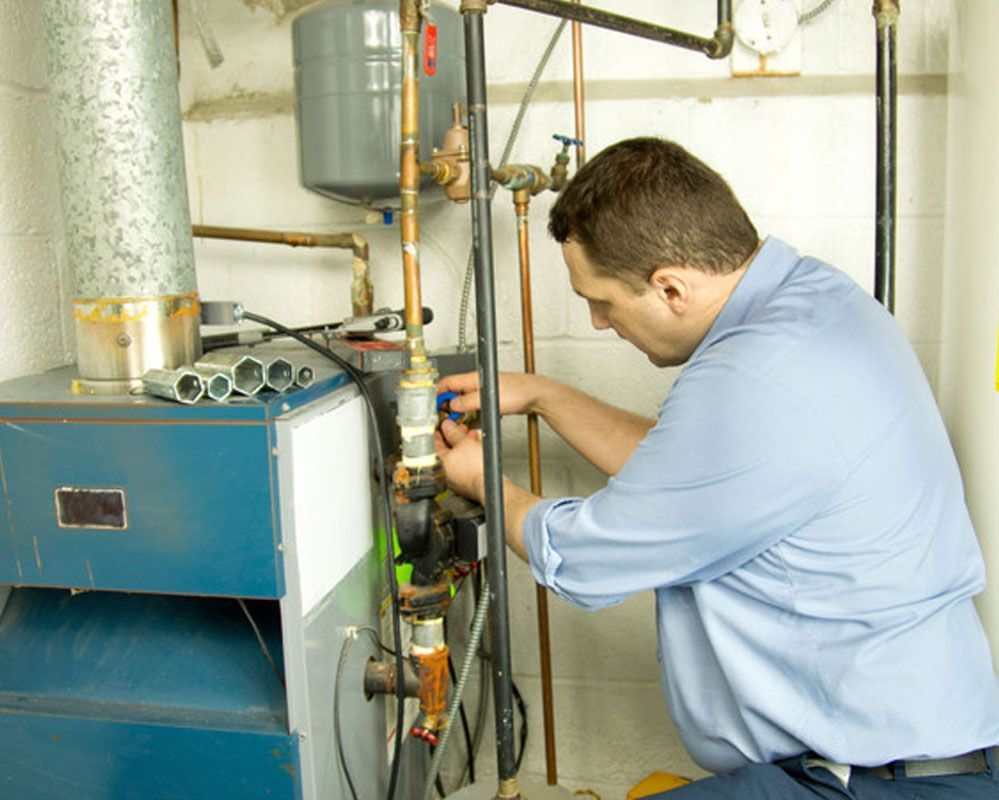 Hand tightening a wrench on a wall-mounted boiler’s exposed pipes and fittings