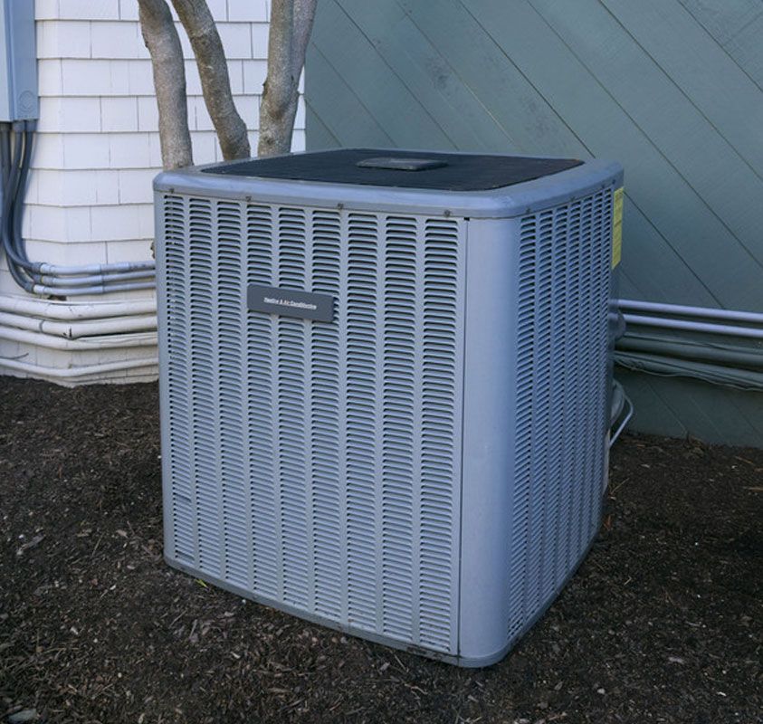 Outdoor HVAC air conditioner unit beside a house, with gray metal siding and pipes nearby