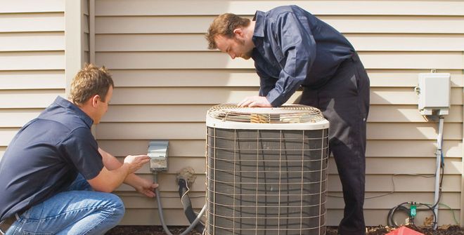 Worker in orange hard hat inspecting rooftop HVAC equipment with a gauge panel