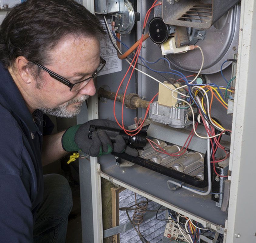 Technician inspecting wiring inside an open HVAC unit, wearing glasses and gloves.