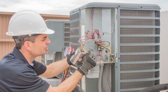 Technician in hard hat repairs rooftop HVAC unit with tools and wiring exposed