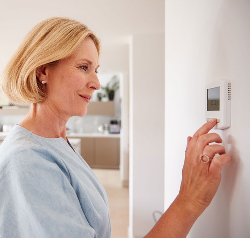 Woman adjusting a wall thermostat in a bright home interior