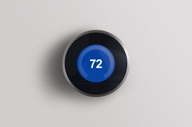 Round black smart thermostat displaying 72° on a white wall