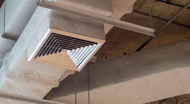 White ceiling vent grille and ductwork inside an unfinished industrial space