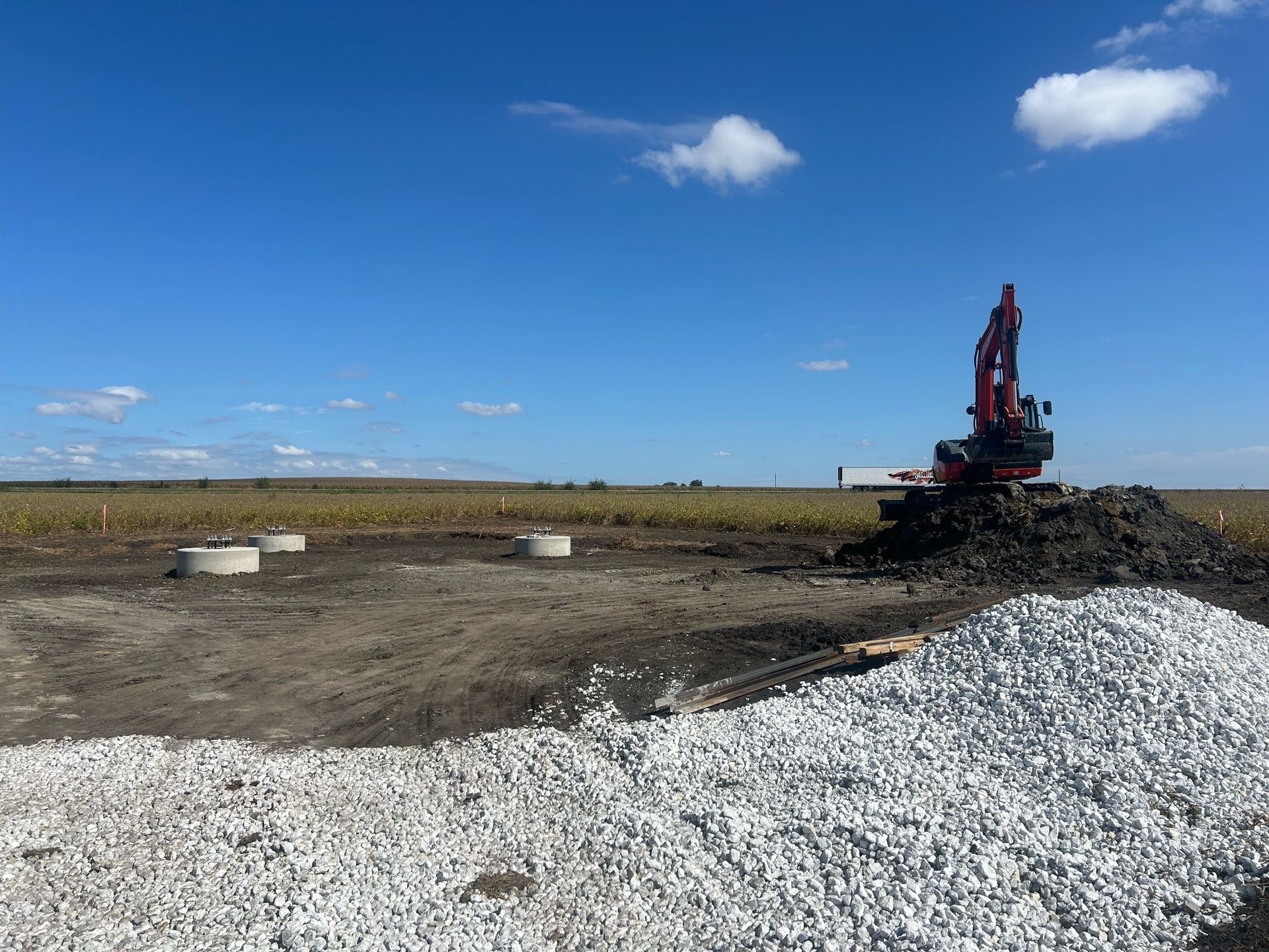 A red excavator is sitting on top of a pile of gravel in a field