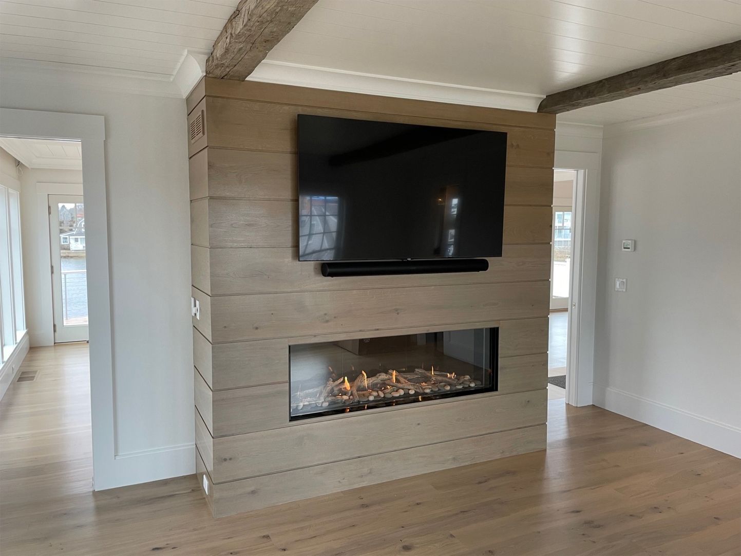 Fireplace with TV mounted above, in a light wood-paneled wall, light wood floor, bright room.