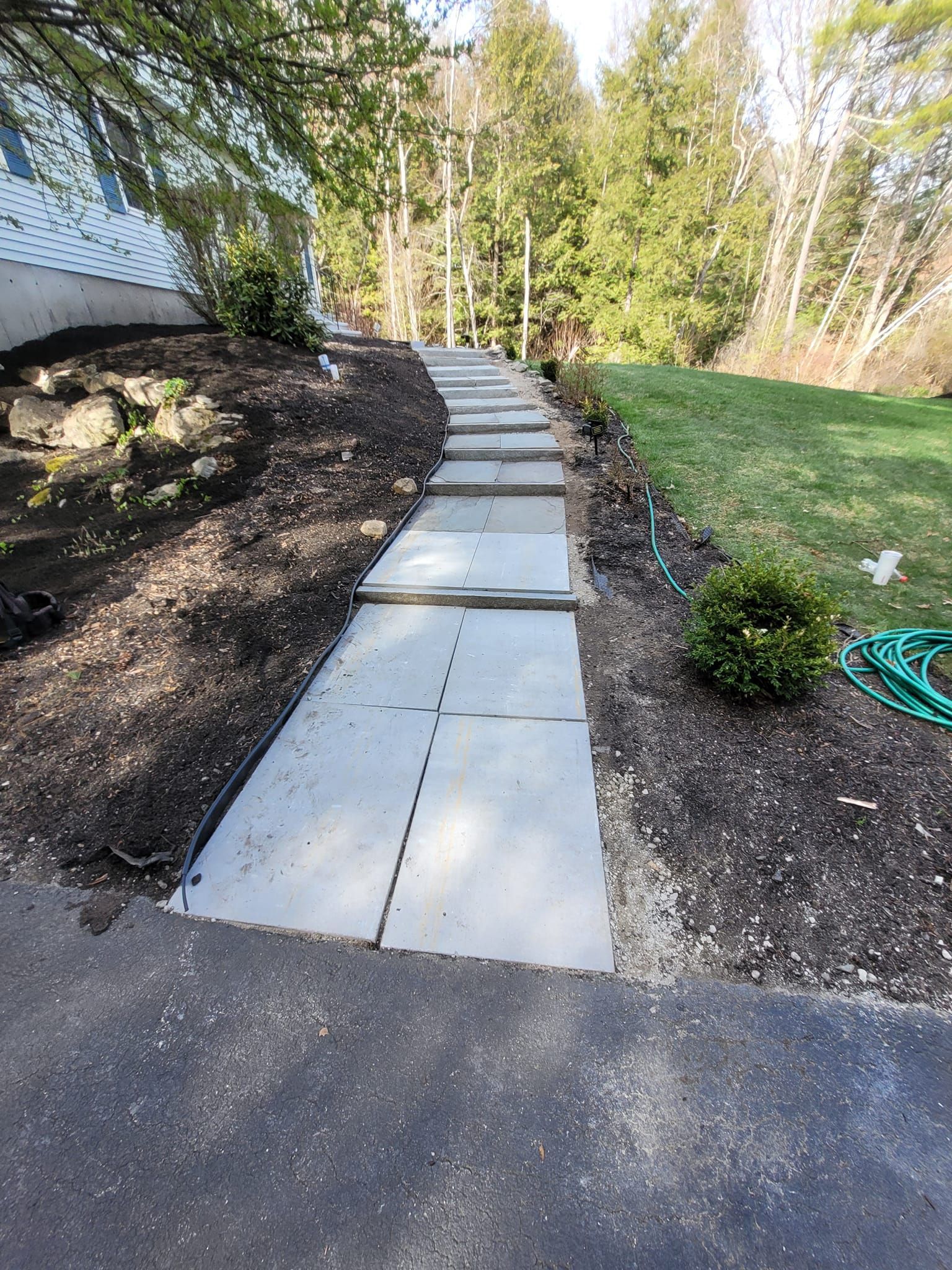 A concrete walkway leading to a house with a hose on the side of it.