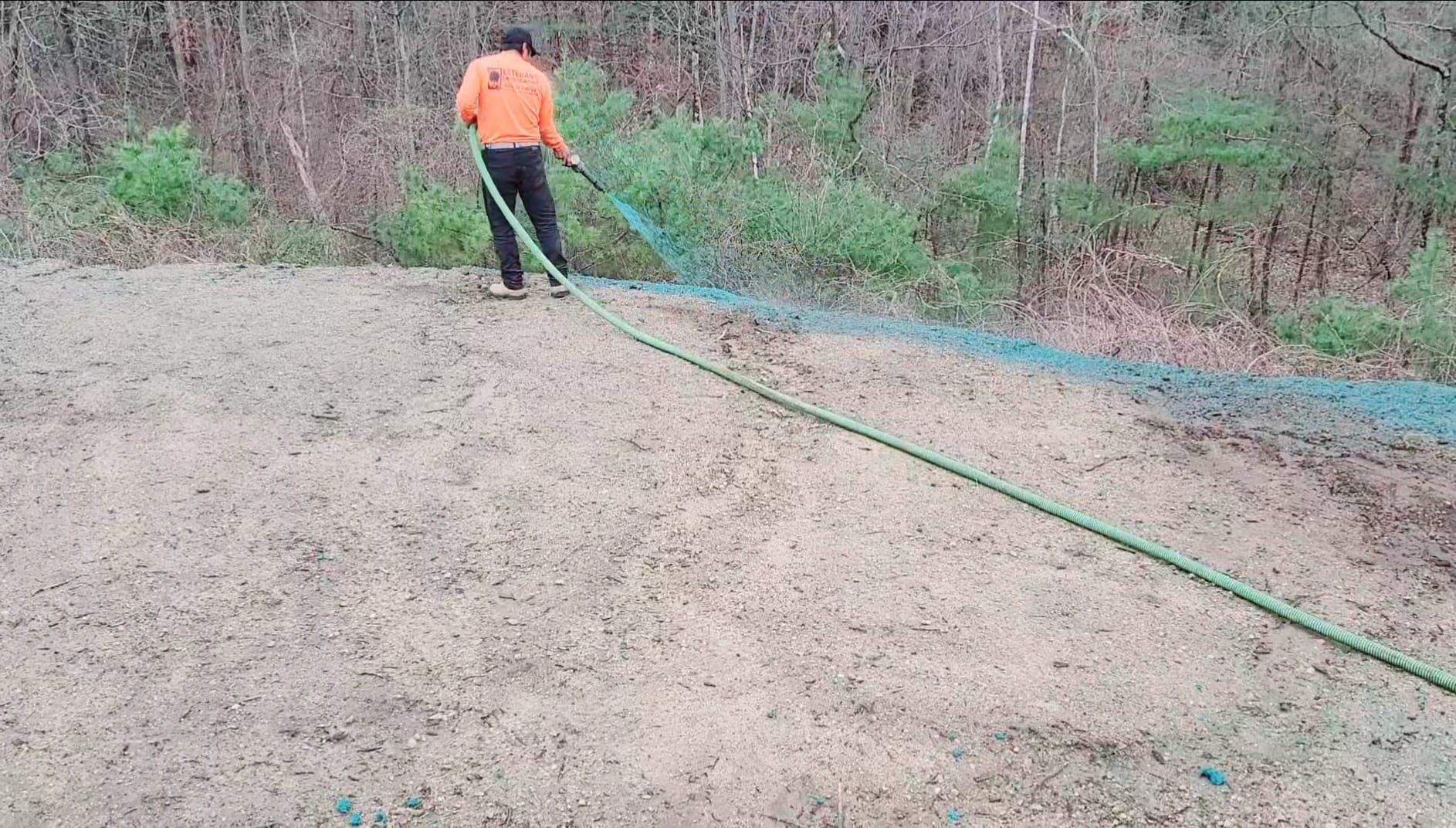 A man is using a hose to water a dirt field.