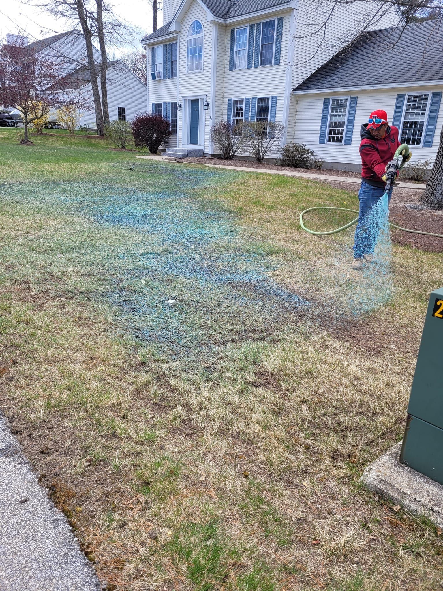 A man is spraying green fertilizer on a lawn in front of a house.