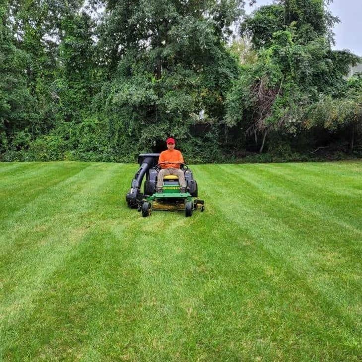 A man is riding a lawn mower on a lush green lawn.