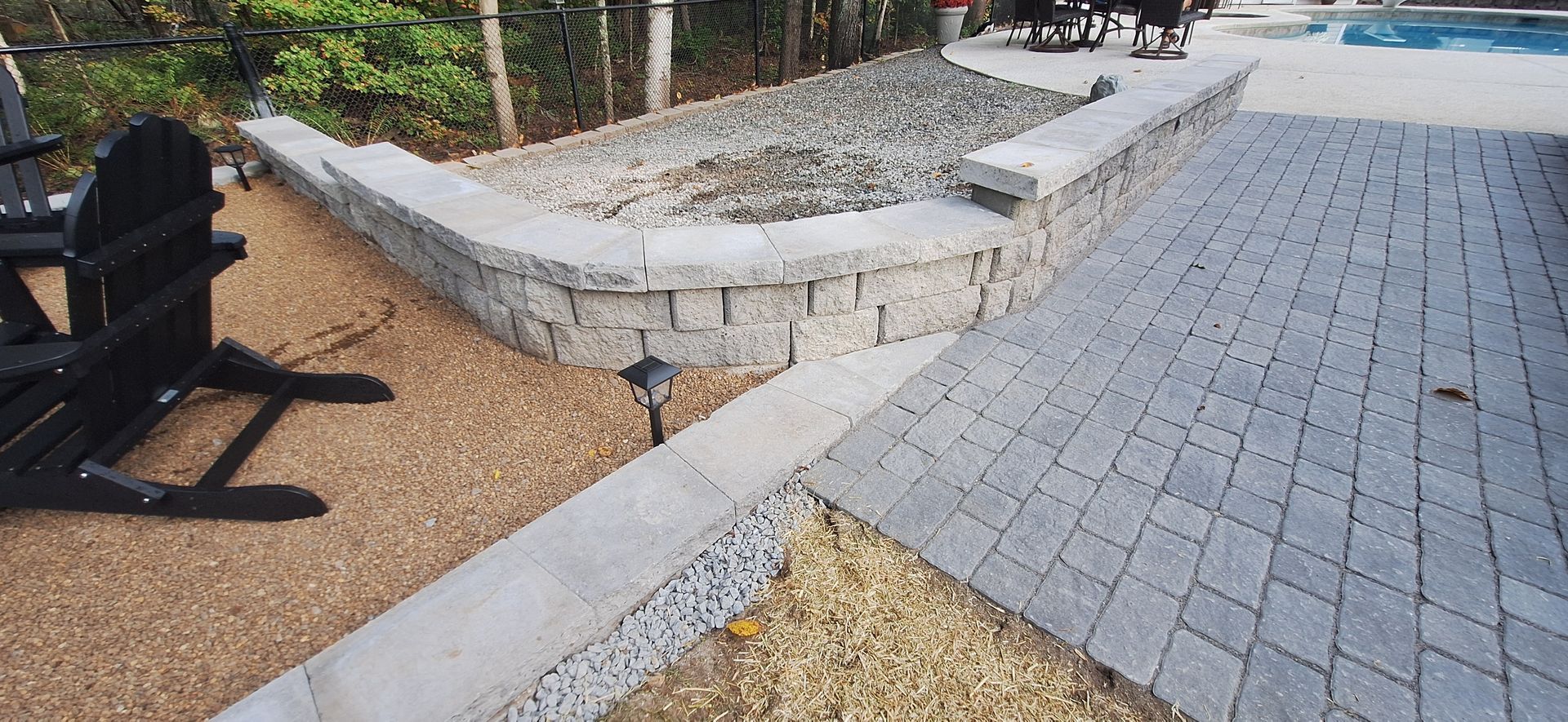 A patio with chairs and a wall next to a pool.