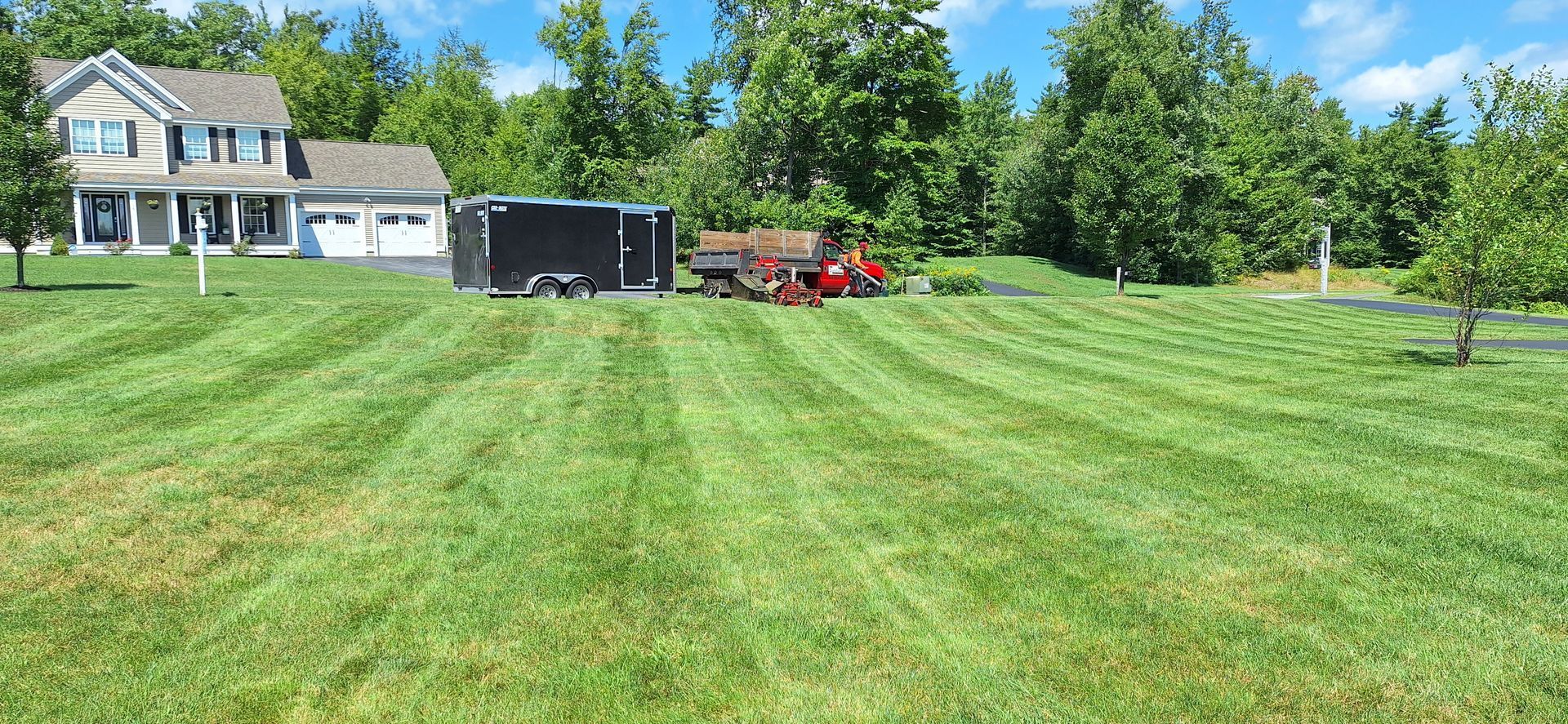 A lawn mower is cutting a lush green lawn in front of a house.