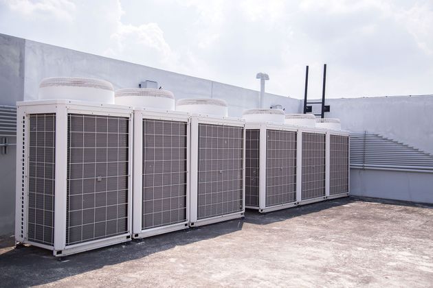 Row of large outdoor HVAC units beside a white building under bright daylight