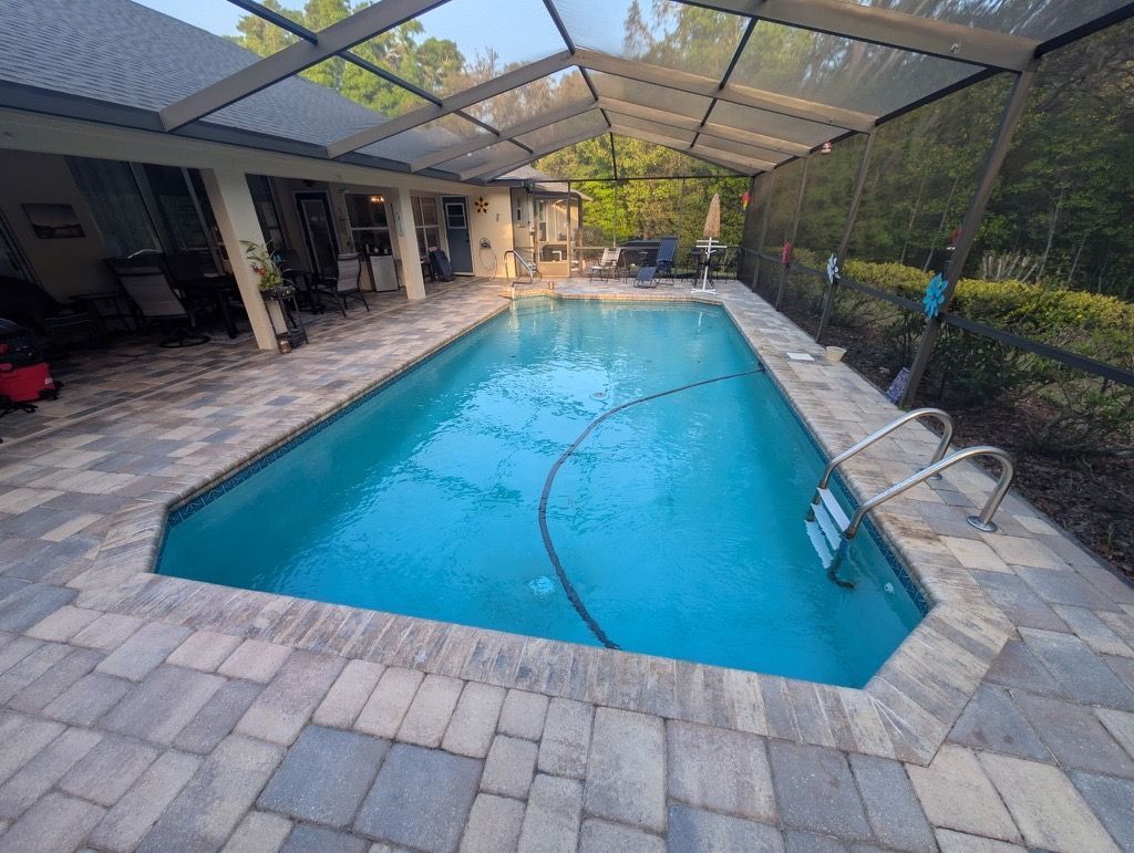 Backyard swimming pool under a screened lanai, with blue water and stone paver decking