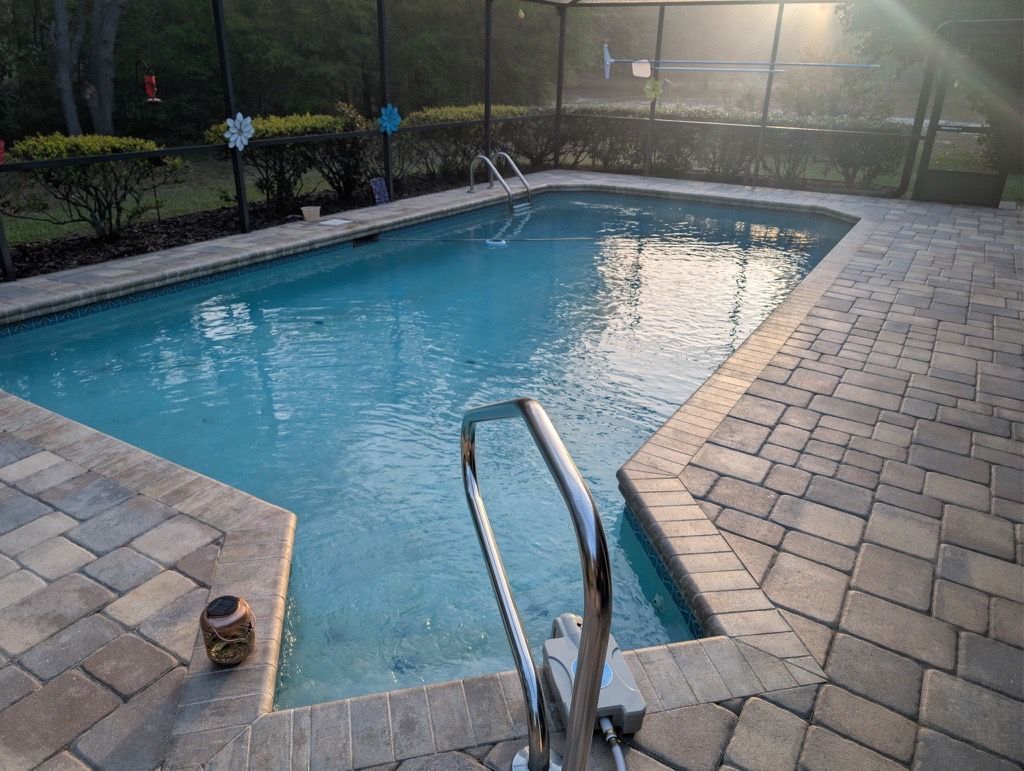 Backyard swimming pool with brick patio and metal handrail at sunset