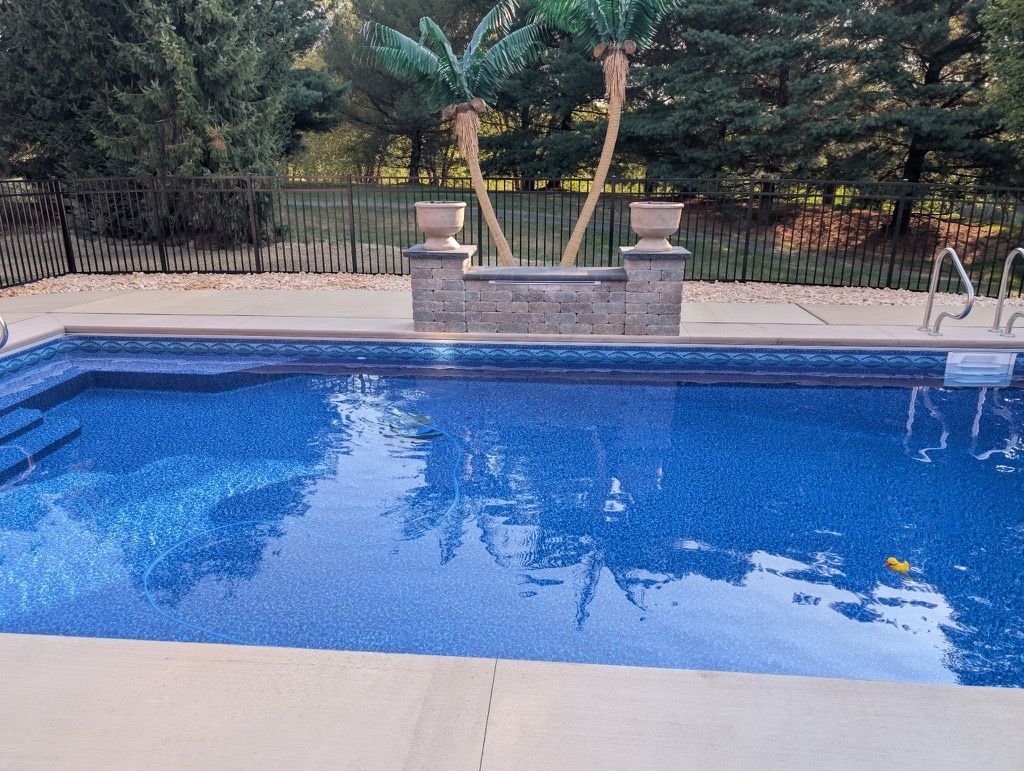 Blue backyard swimming pool with a stone planter and trees in the background