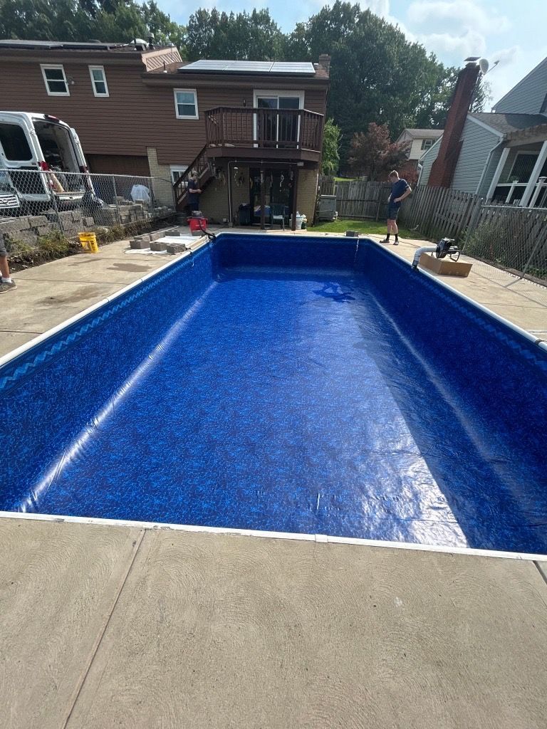 Blue rectangular in-ground swimming pool in a backyard, viewed from the shallow end.