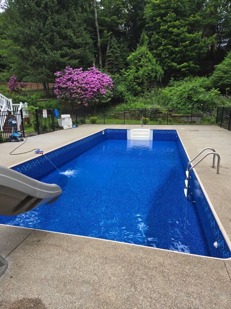 Backyard swimming pool with blue water, slide, and metal handrail beside a lush green garden
