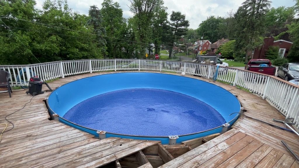 Above-ground blue pool on a wooden deck with white railing in a backyard
