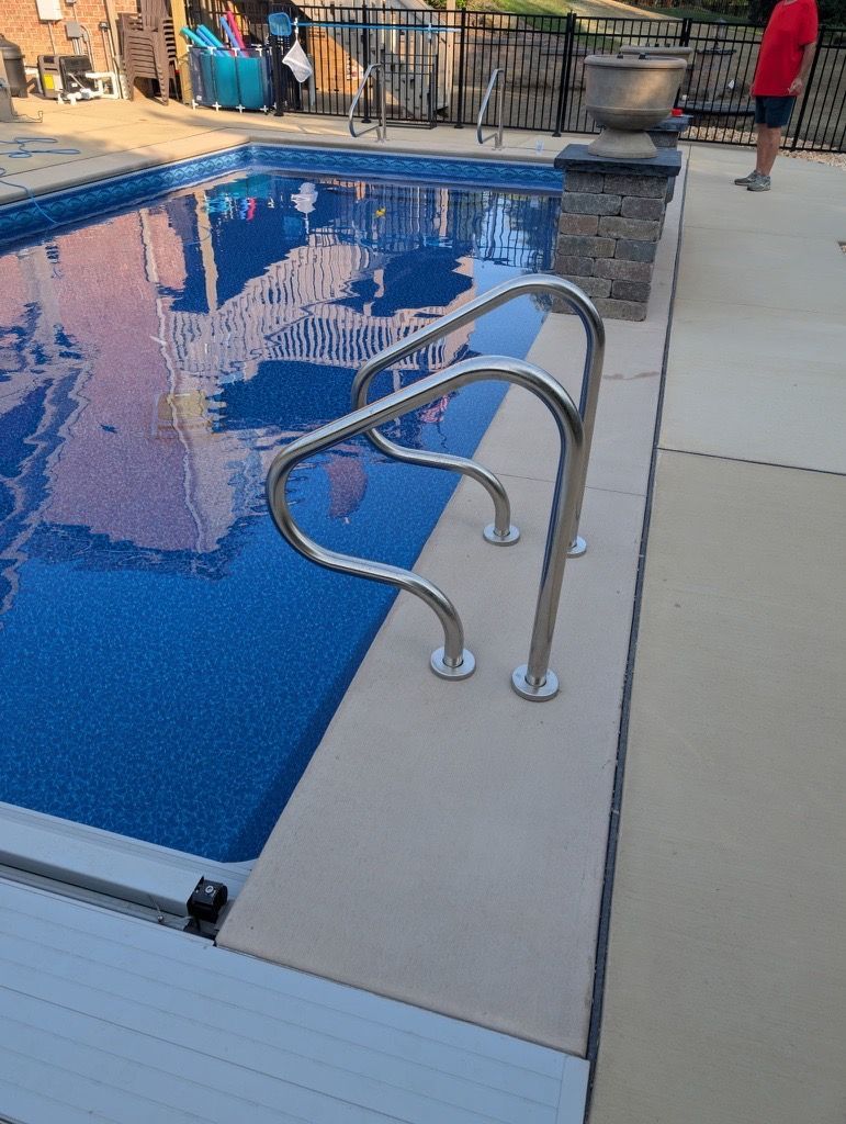 Swimming pool ladder beside a blue pool, with people gathered in the background and a concrete deck.