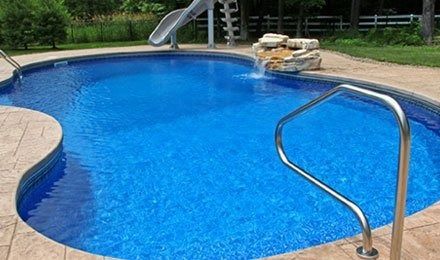 Backyard swimming pool with blue water, slide, and stainless steel ladder on a stone deck