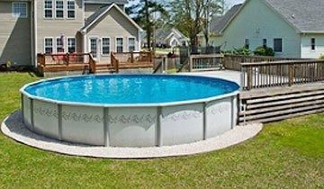 Above-ground pool in a backyard with a wooden deck and houses in the background