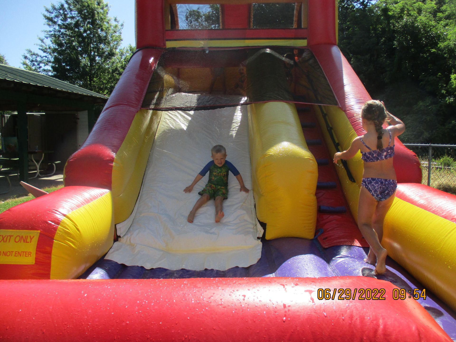 A girl in a bikini is standing next to a boy on an inflatable slide