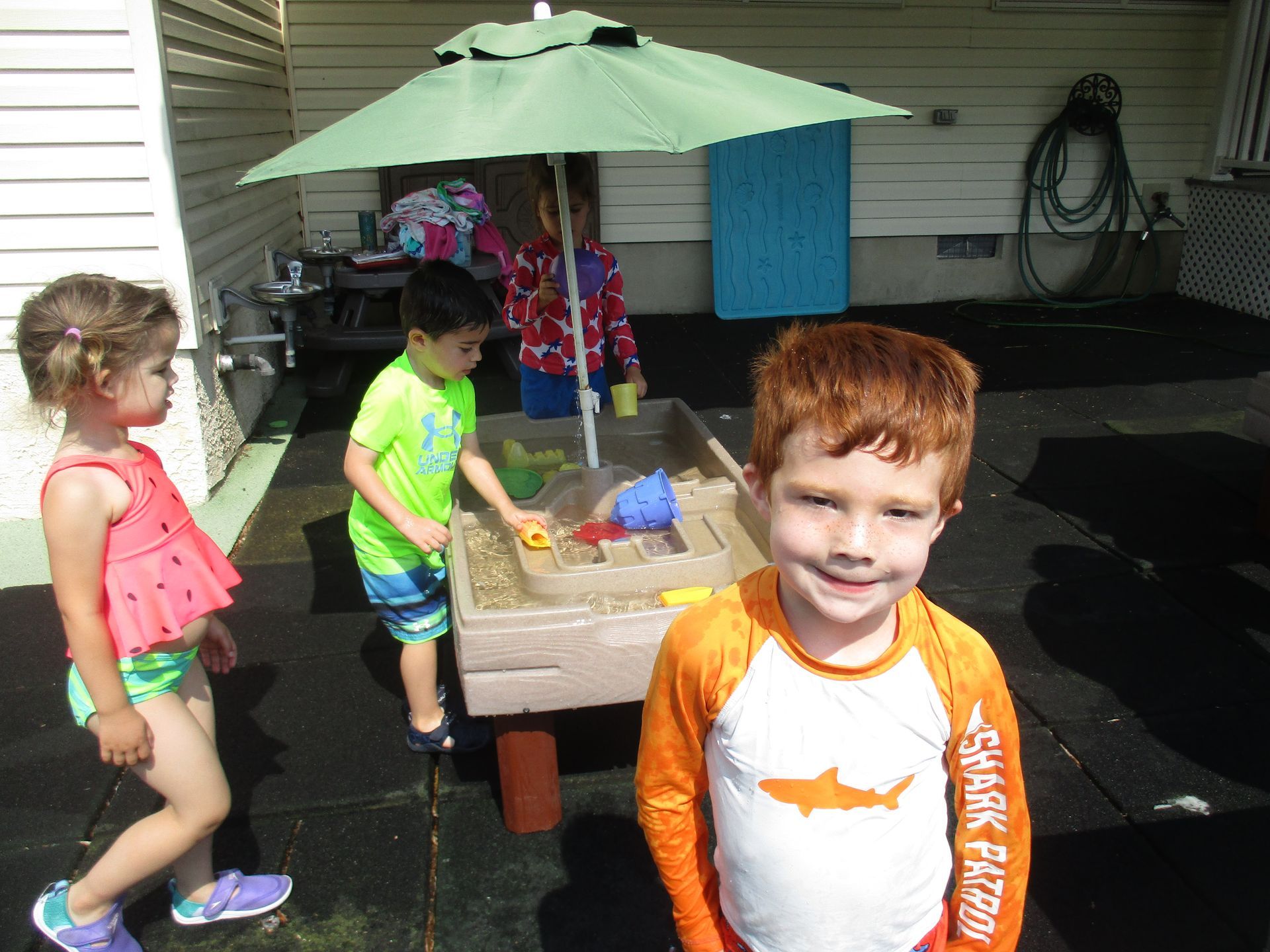 A group of children are playing in a sandbox under an umbrella.