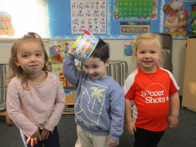 A boy wearing a soccer shots shirt is standing next to two other children