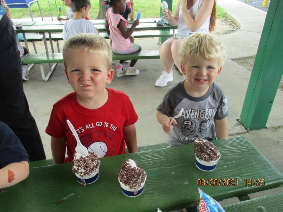Two young boys are sitting at a picnic table eating ice cream.