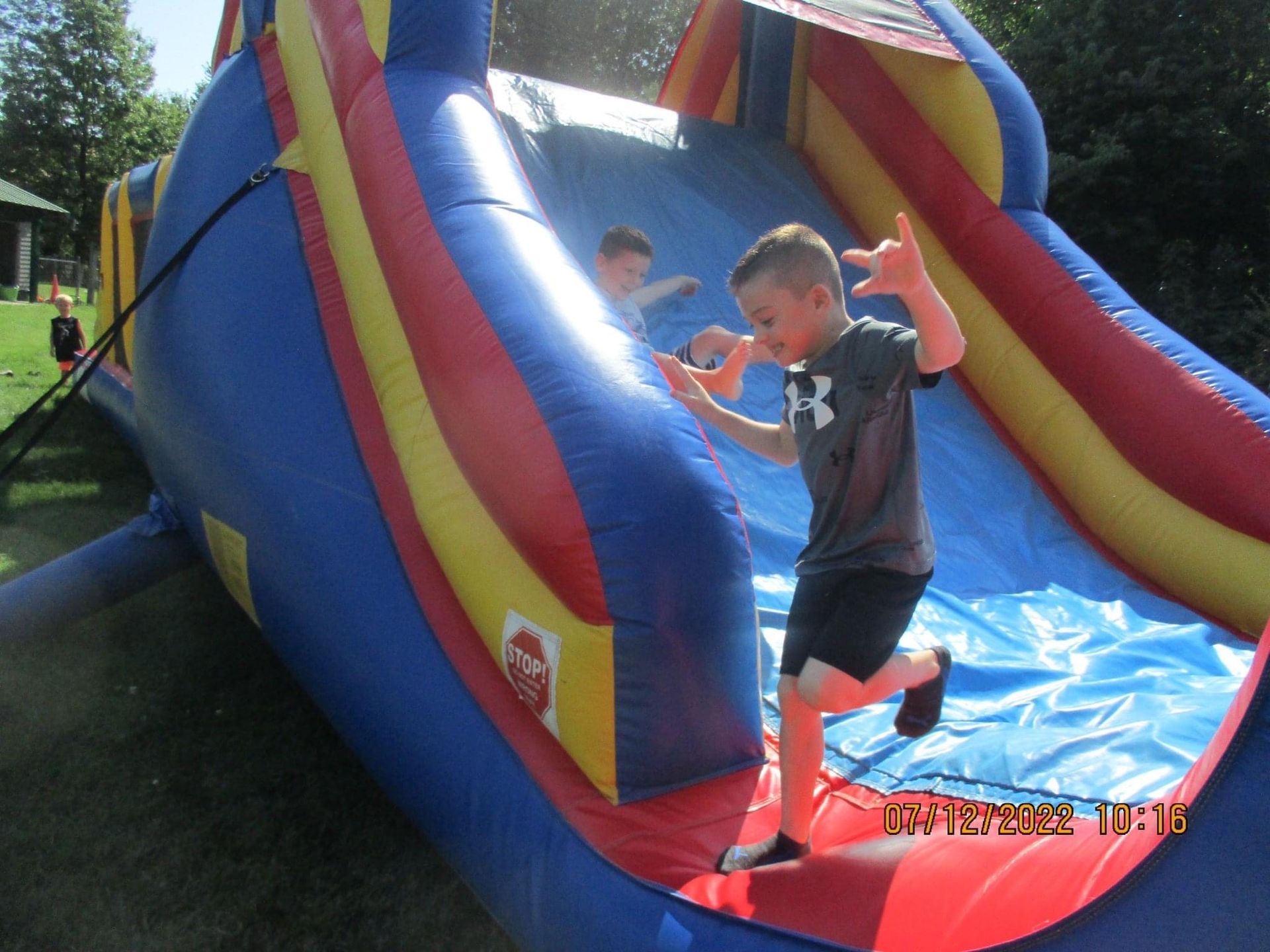 A boy wearing a under armour shirt is playing on an inflatable slide