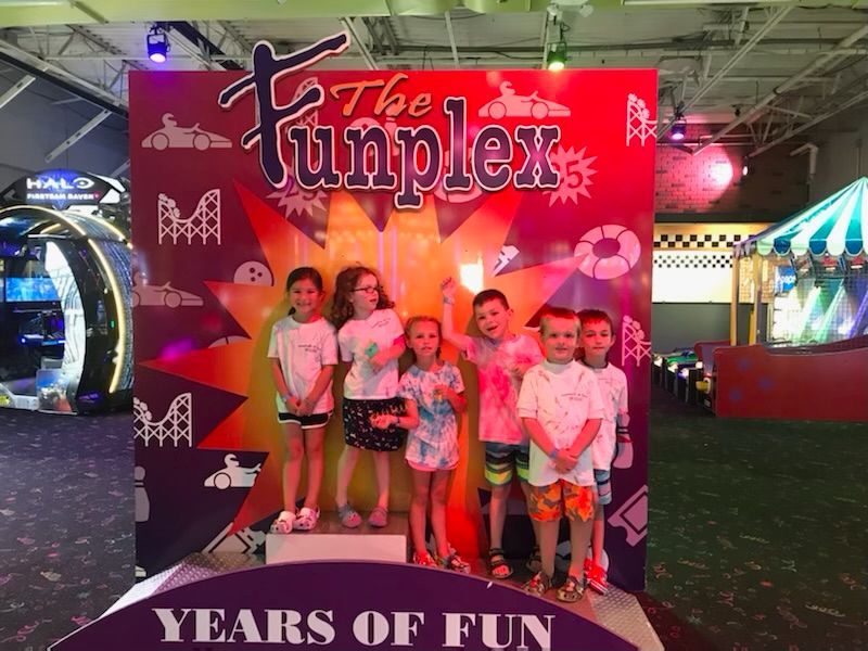 A group of children standing in front of a sign that says the funplex