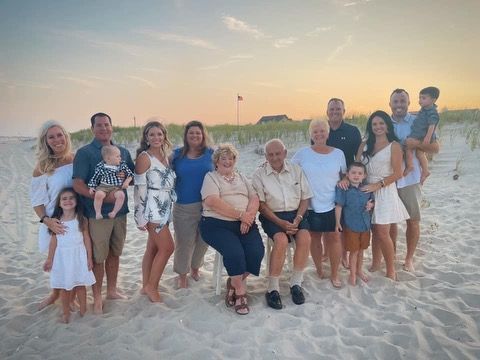 A large family is posing for a picture on the beach.