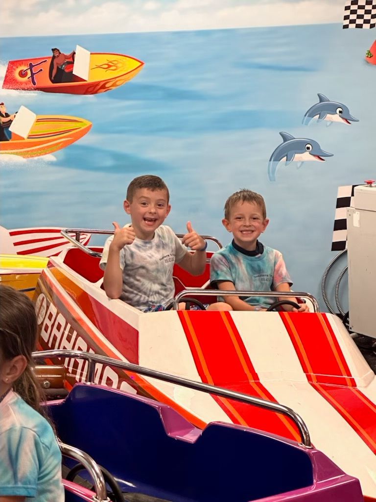 Two young boys are riding a roller coaster and giving a thumbs up.