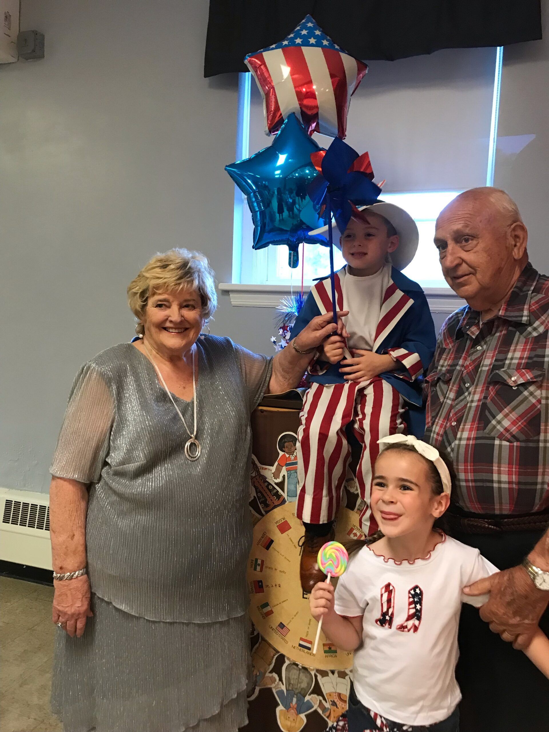 A little girl is holding a lollipop while posing for a picture with her grandparents.