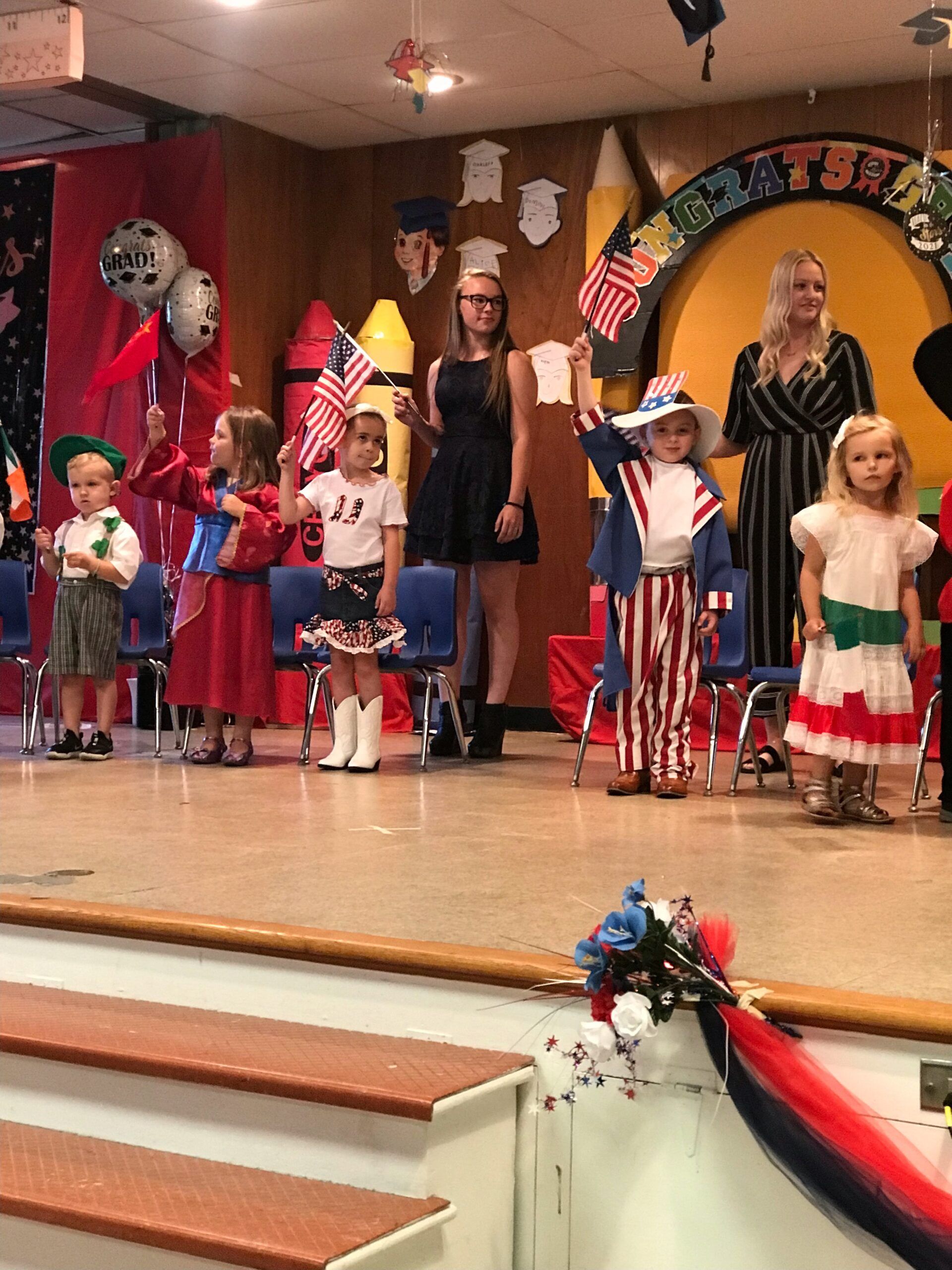 A group of children are standing on a stage holding flags