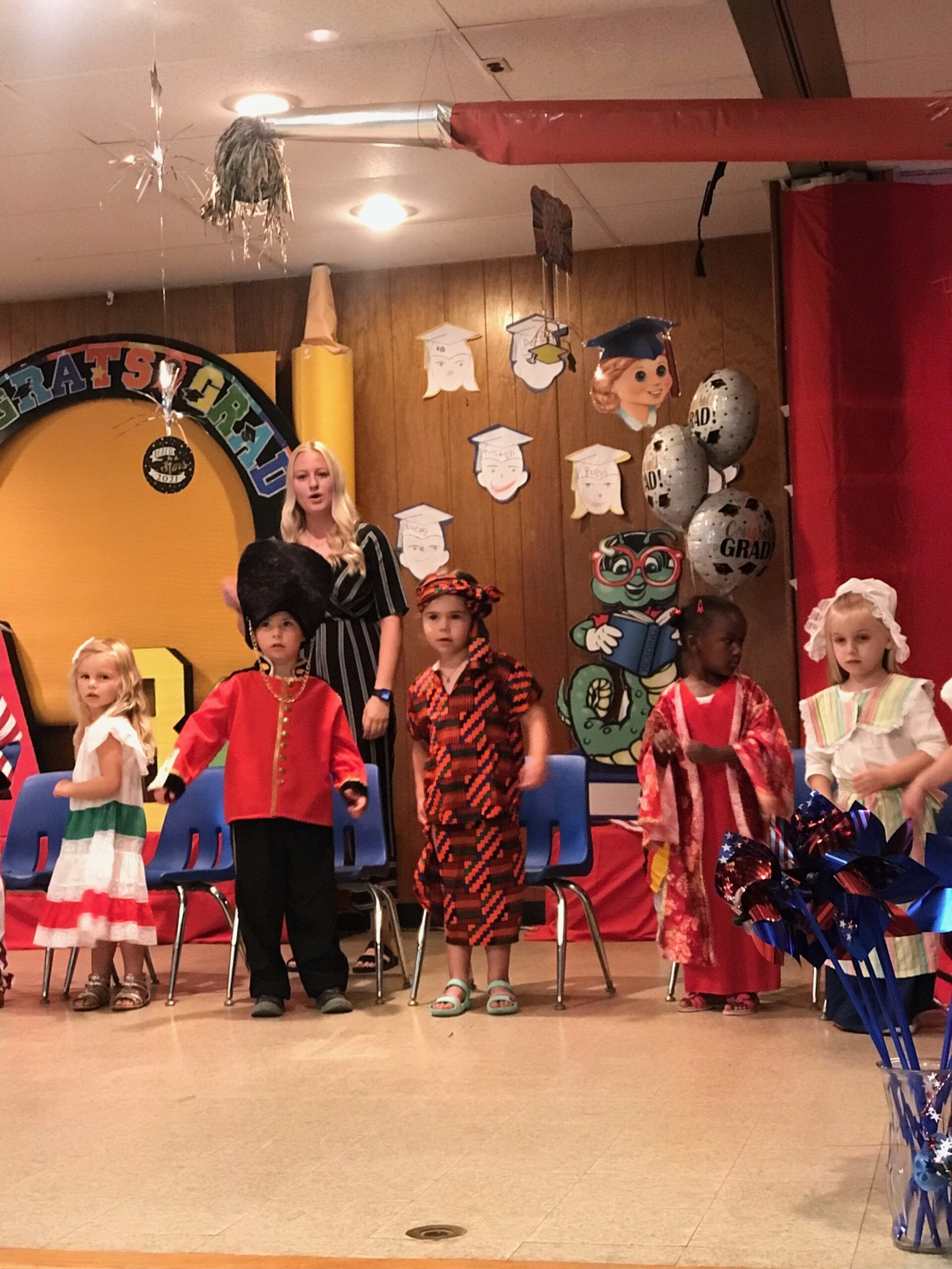 A group of children are standing on a stage in front of a sign that says first