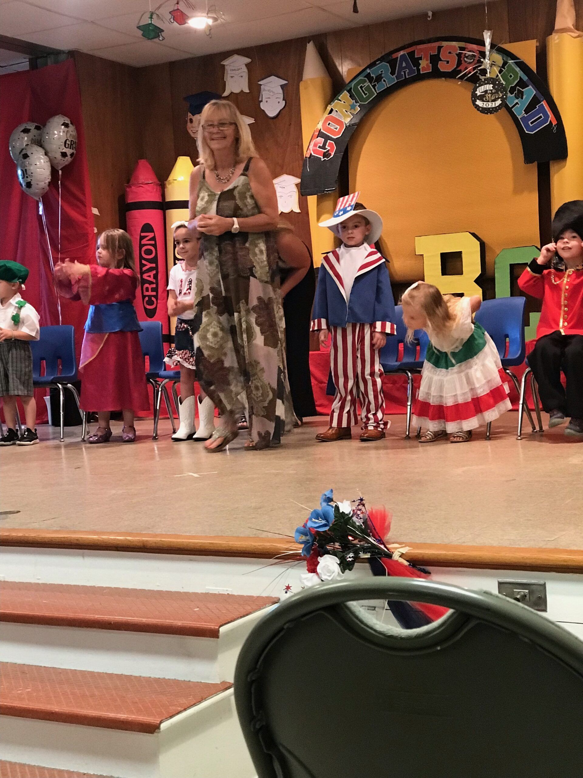 A woman stands on a stage with children in front of a sign that says crayon
