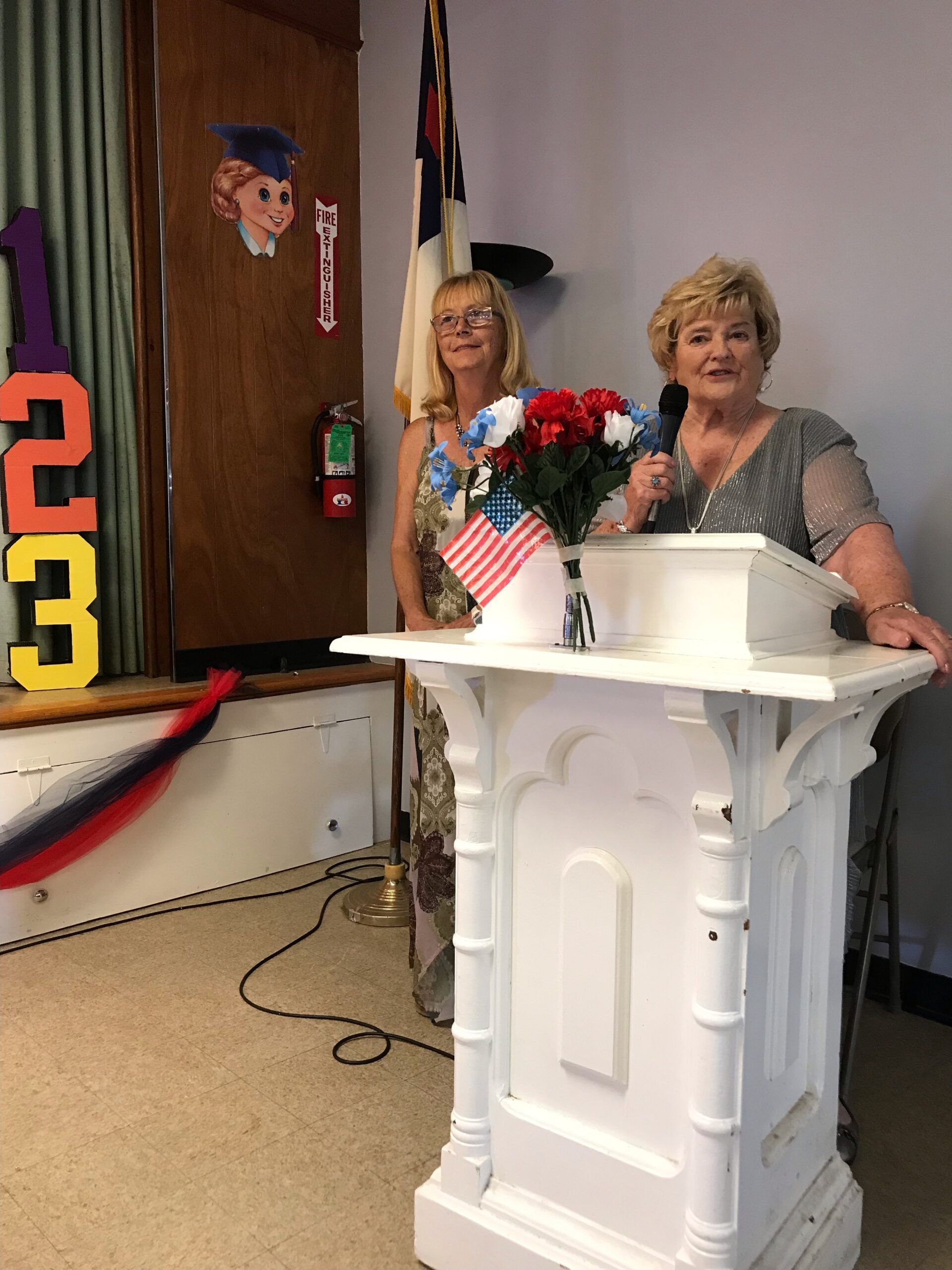 Two women standing behind a podium with the number 33 on the wall behind them