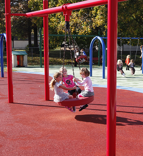 Three little girls are sitting on a swing in a playground