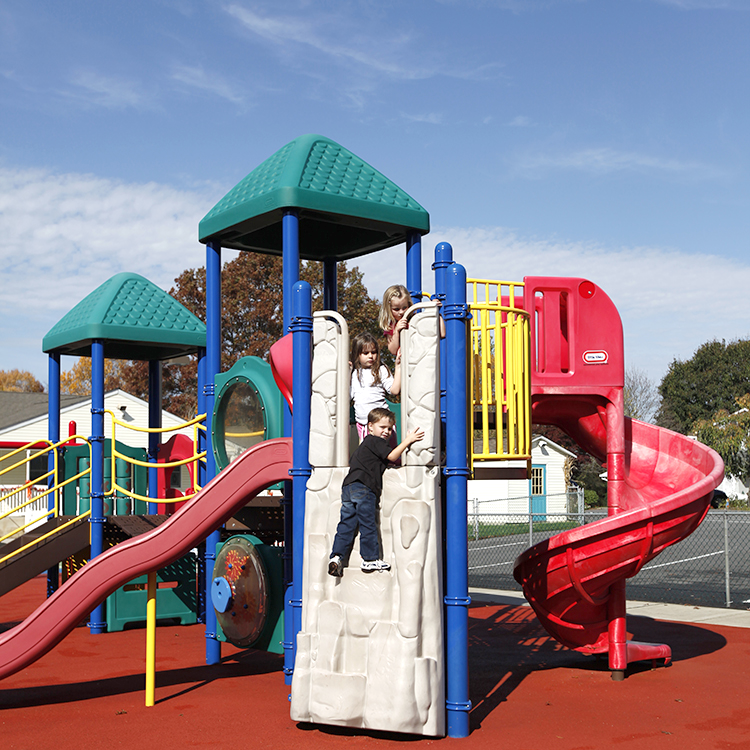 Two children are playing on a playground with a red slide