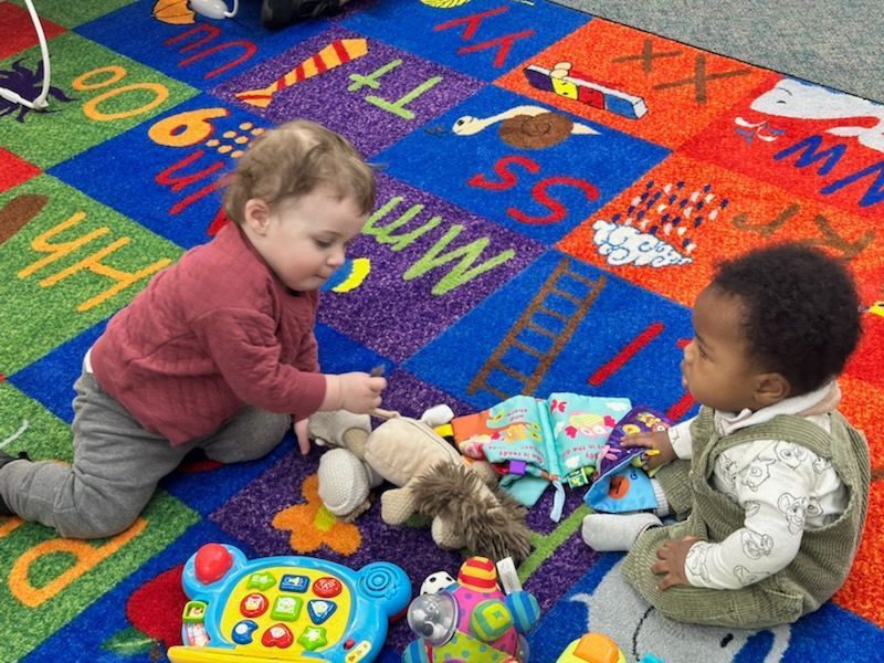 Two toddlers are playing with toys on a rug with letters on it