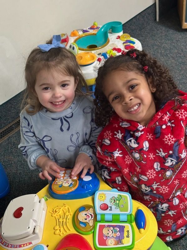 Two little girls are sitting at a table with toys and smiling