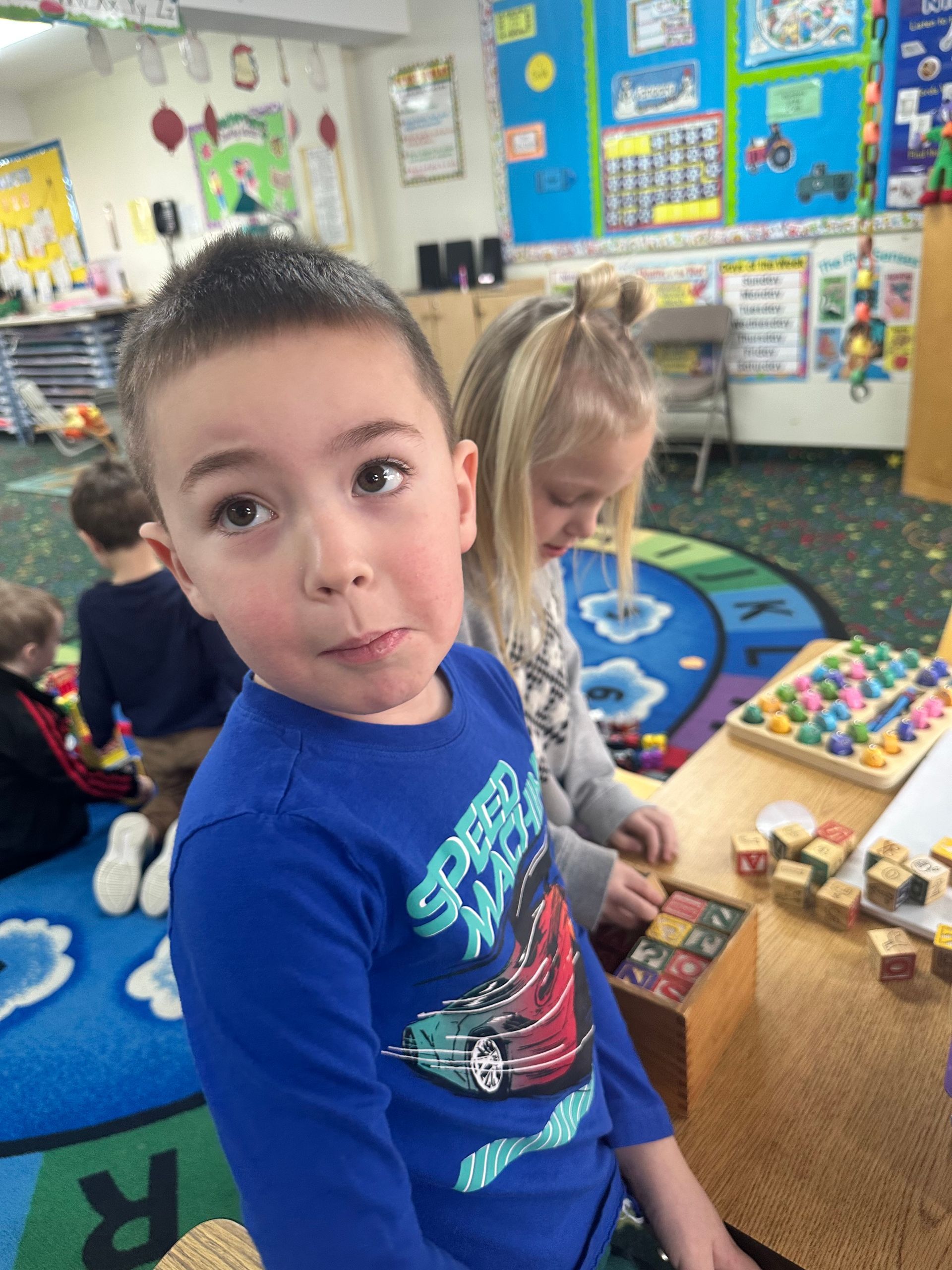 A boy in a blue shirt is sitting at a table in a classroom.
