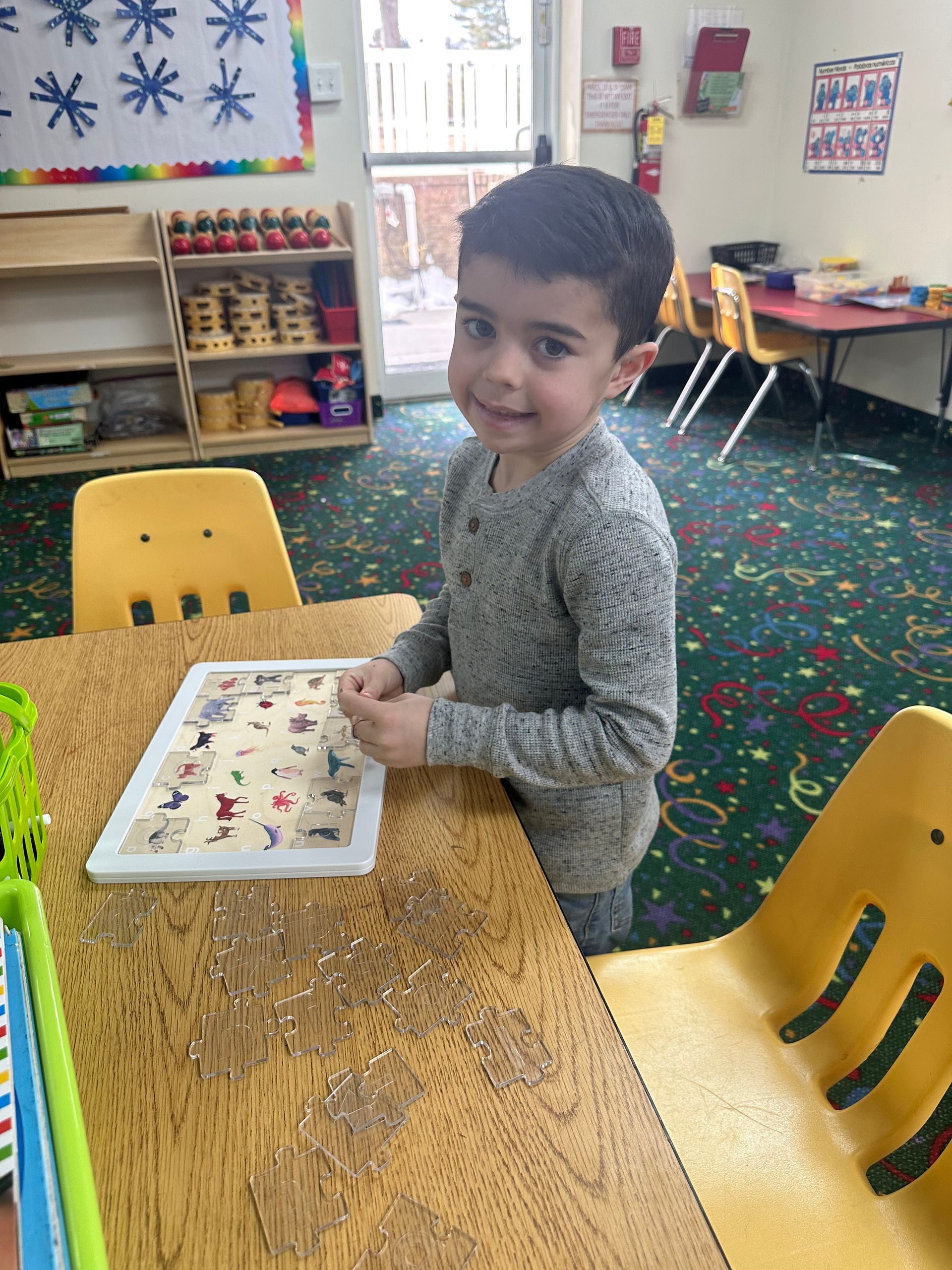 A young boy is sitting at a table in a classroom playing with a tablet.