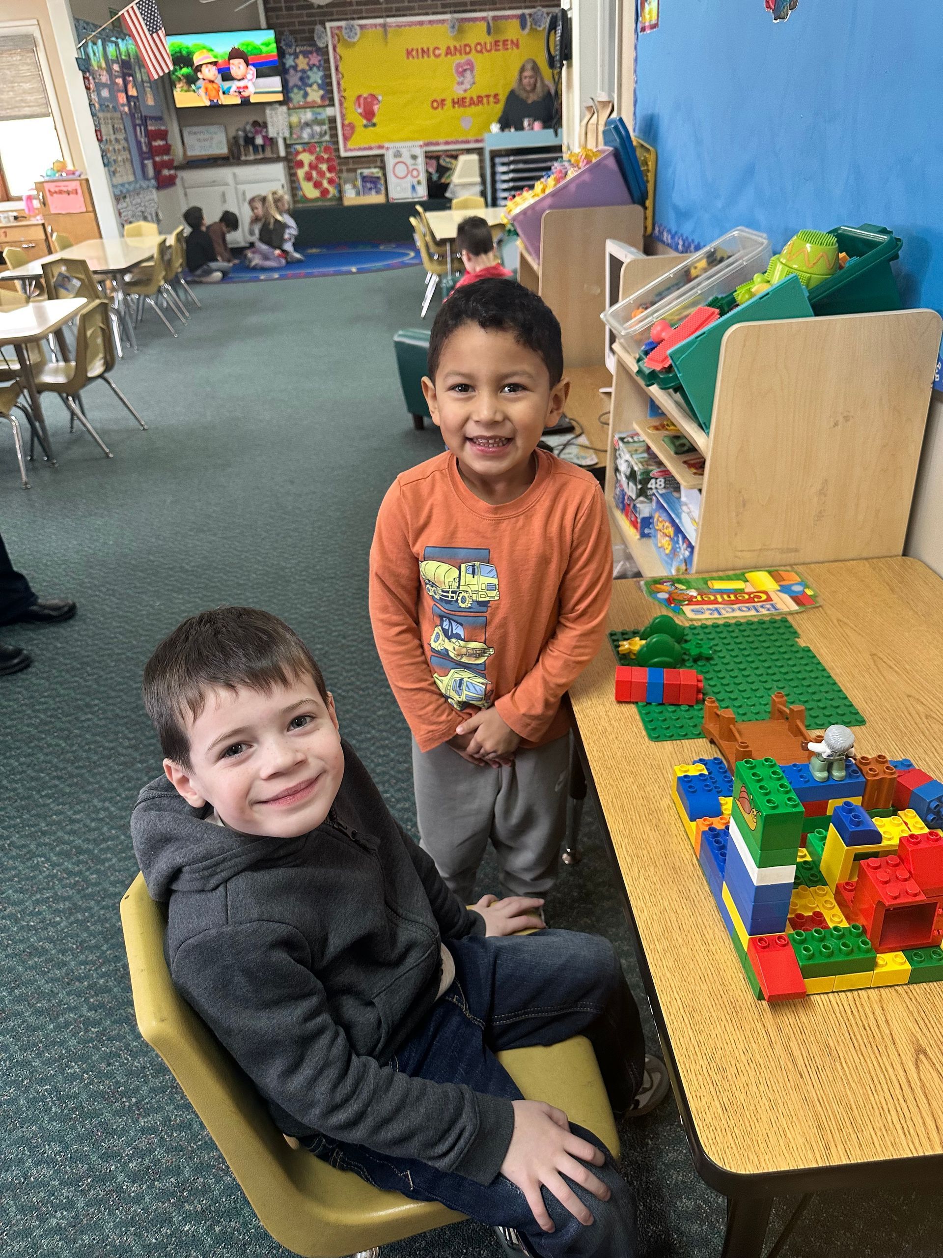 Two young boys are playing with lego blocks in a classroom.