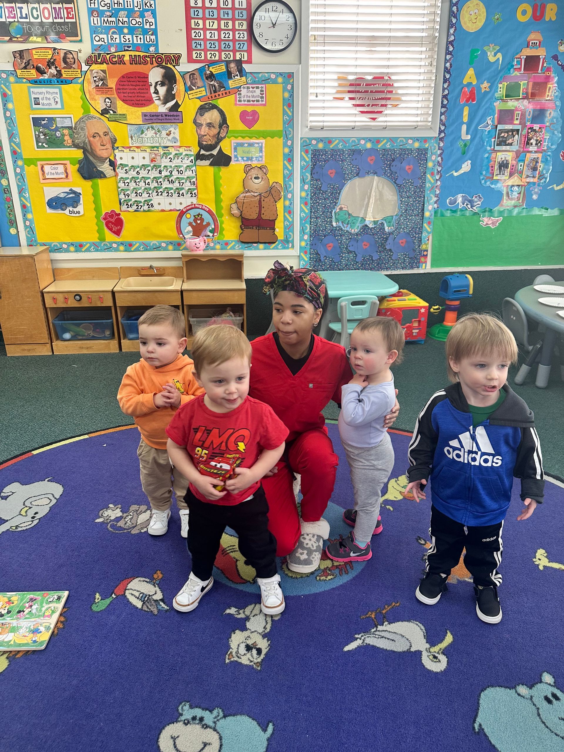A group of children are standing around a woman in a classroom.