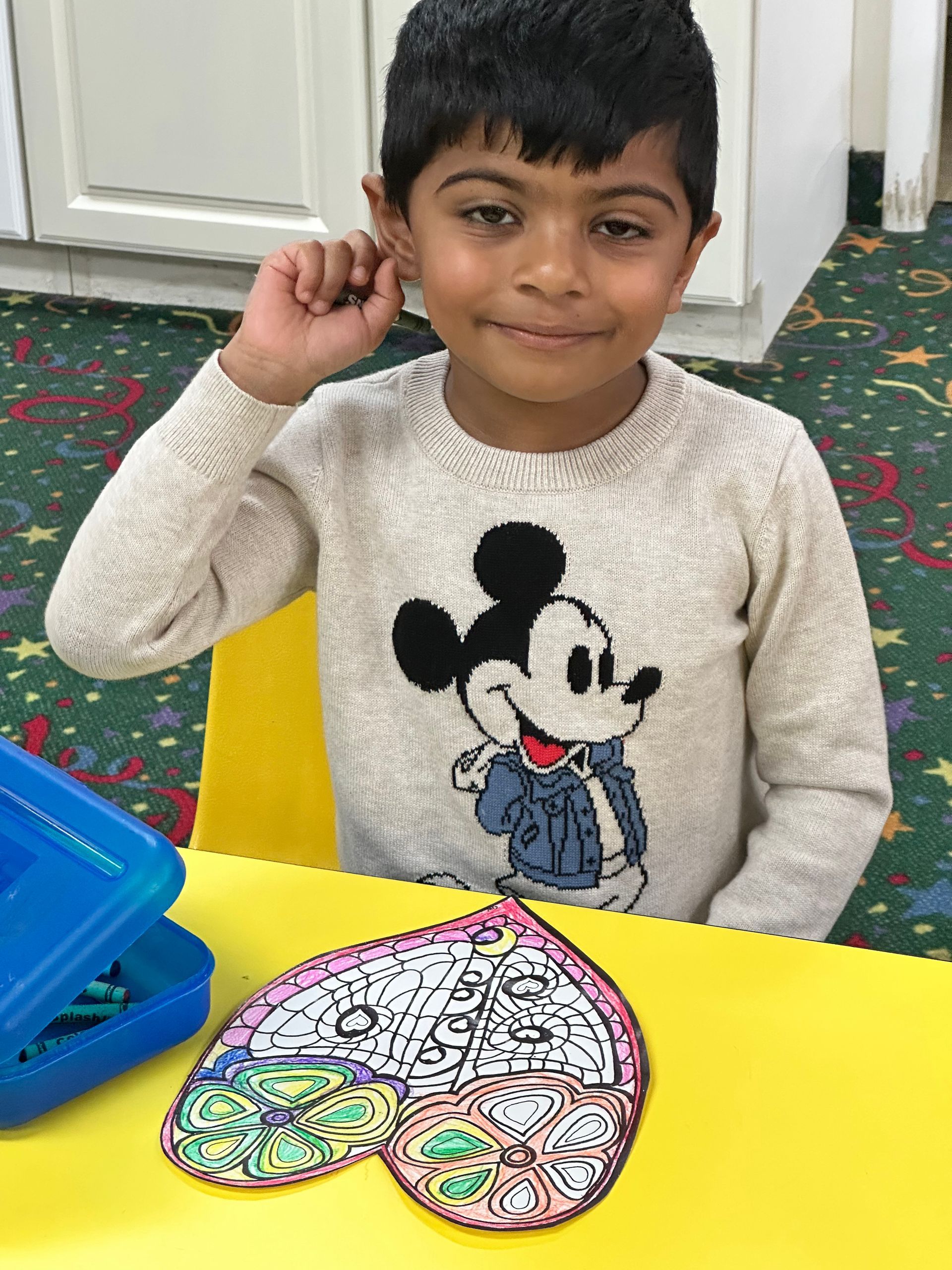 A young boy wearing a mickey mouse sweater sits at a table