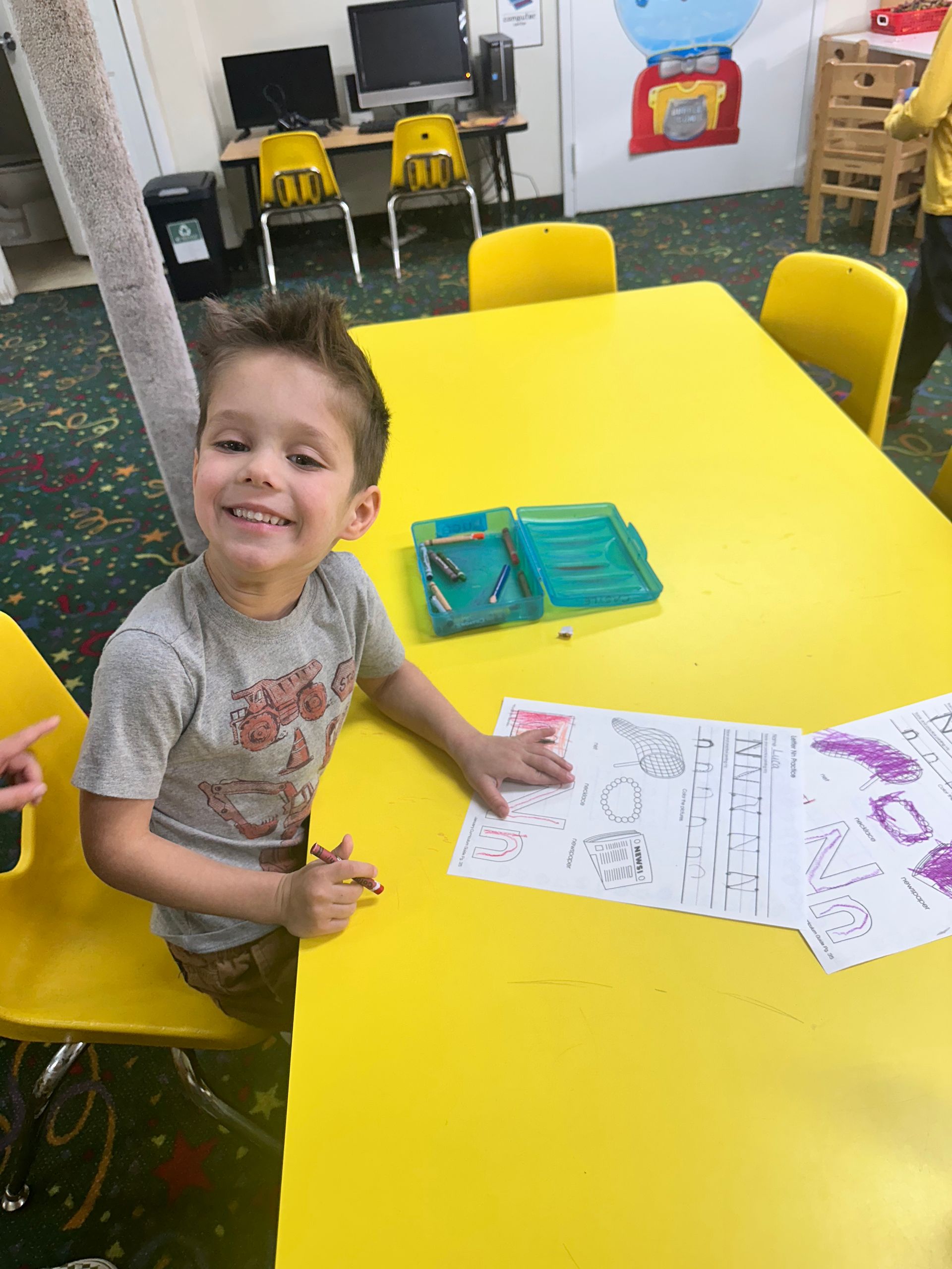 A young boy is sitting at a yellow table drawing on a piece of paper.